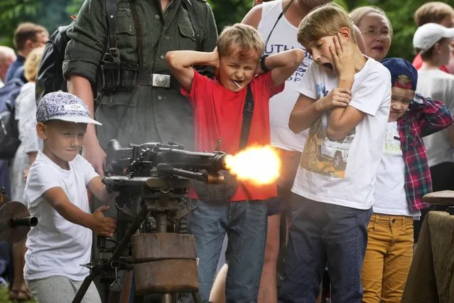 A boy shoots a World War II ages machine gun with blanks at a weapon exhibition during a military show in St. Petersburg, Russia, Sunday, July 10, 2022. (Photo by Dmitri Lovetsky/AP Photo)