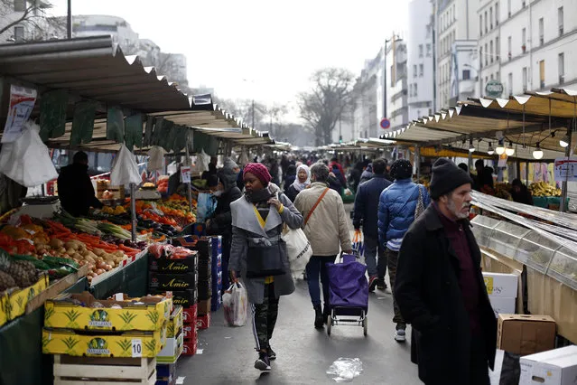 People walk in the open air market of Belleville, in Paris, Friday, March 20, 2020. French President Emmanuel Macron said that for 15 days starting at noon on Tuesday, people will be allowed to leave the place they live only for necessary activities such as shopping for food, going to work or taking a walk. (Photo by Thibault Camus/AP Photo)