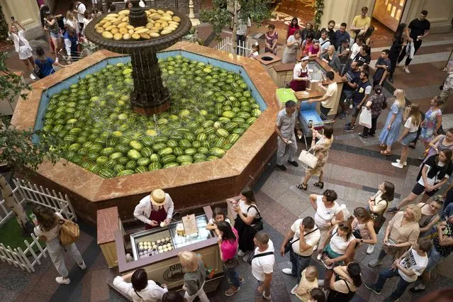 Customers and tourists line up to buy an ice-cream near a fountain decorated with Astrakhan watermelons and Asian melons inside the GUM department store in Moscow, Russia, Sunday, August 7, 2022. Markets selling Astrakhan watermelons and Asian melons traditionally open in Moscow in August. (Photo by Alexander Zemlianichenko/AP Photo)