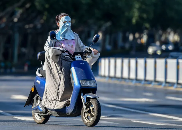 A woman rides an electric bicycle on her way as she wears a sunscreen mask towards off strong ultraviolet rays in Fuyang, China on August 14, 2022. The Central Meteorological Observatory of China issued a high-temperature red warning. It is expected that the maximum temperature in some parts of China will reach above 40°C on August 14. (Photo by Sheldon Cooper/SOPA Images/Rex Features/Shutterstock)