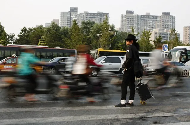 Zhang Guanhui, impersonating Michael Jackson, waits to cross a street as he heads  downtown for his street performance in Beijing August 20, 2014. Zhang, born in 1984, quit elementary school and has since held jobs as a factory worker, waiter, and security guard. After watching a Michael Jackson music video four years ago for the first time, Zhang says he became fascinated and now puts on shows on the street and small stages impersonating the King of Pop. (Photo by Kim Kyung-Hoon/Reuters)