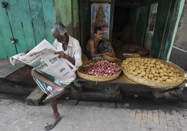 A local resident reads a newspaper next to a vendor selling potatoes and onions at a slum area in Kolkata, India, September 4, 2015. (Photo by Rupak De Chowdhuri/Reuters)