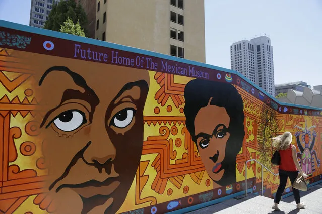 In this photo taken Wednesday, July 13, 2016, a woman walks past a mural outside the future home of the Mexican Museum under construction in San Francisco. (Photo by Eric Risberg/AP Photo)