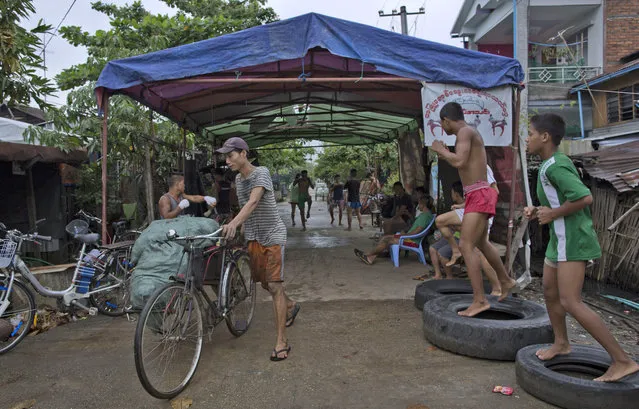 In this Tuesday, July 14, 2015, photo, members of the White New Blood lethwei fighters club, a Myanmar traditional martial-arts club which practices a rough form of kickboxing, warm up in their gym on a street as a man pushes his rickshaw with a load of charcoal in Oakalarpa, north of Yangon, Myanmar. (Photo by Gemunu Amarasinghe/AP Photo)