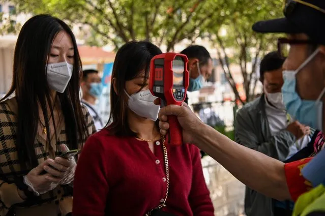 A worker wearing a face mask checks passengers body temperatures and a health code on their phones before they take a taxi after arriving at Hankou railway station in Wuhan, Hubei Province on May 12, 2020. China reported no new domestic coronavirus infections on May 12, after two consecutive days of double-digit increases, including a new cluster over the weekend in Wuhan, which fuelled fears of a second wave of infections. (Photo by Hector Retamal/AFP Photo)