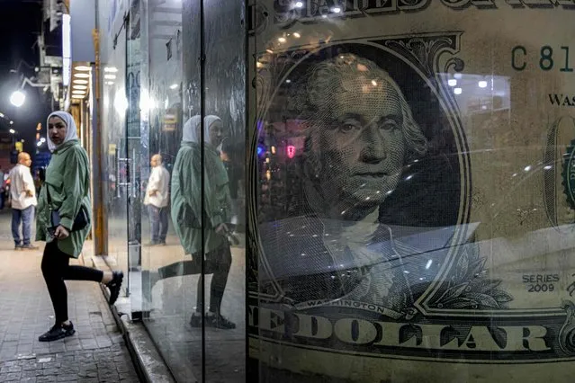 A woman walks out of a currency exchange shop displaying a giant US dollar banknote in the Zamalek district of Egypt's capital Cairo on August 24, 2022. Depleted foreign currency reserves are casting a shadow on Egyptian streets, with the government moving to dim lights to free up energy for export. More natural gas exports means more hard currency, a dire need as experts say a new loan from the International Monetary Fund (IMF) – and an adjacent currency liberalisation – is inevitable. (Photo by Khaled Desouki/AFP Photo)