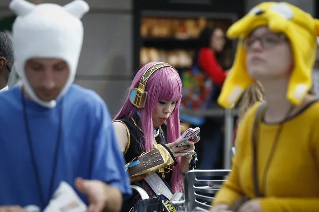 Katie Fang, dressed as a Vocaloid character, looks at her phone near costumed attendees inside New York's Comic-Con convention, October 9, 2014. (Photo by Shannon Stapleton/Reuters)