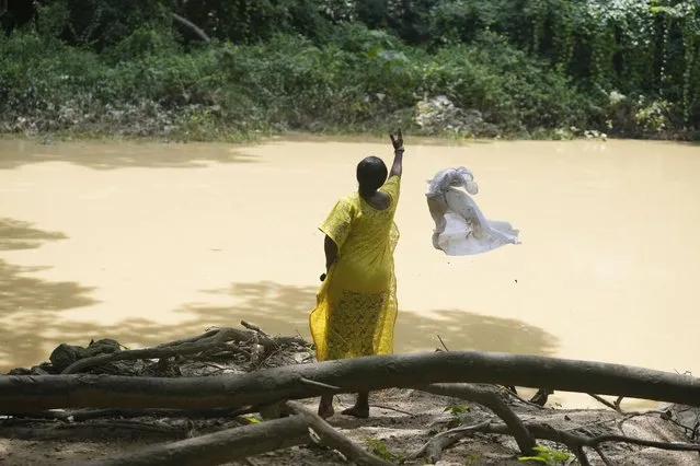 A devotee of the Osun River goddess throws a white cloth used for sacrifices into the sacred waters in Osogbo, Nigeria, on Sunday, May 29, 2022. (Photo by Sunday Alamba/AP Photo)