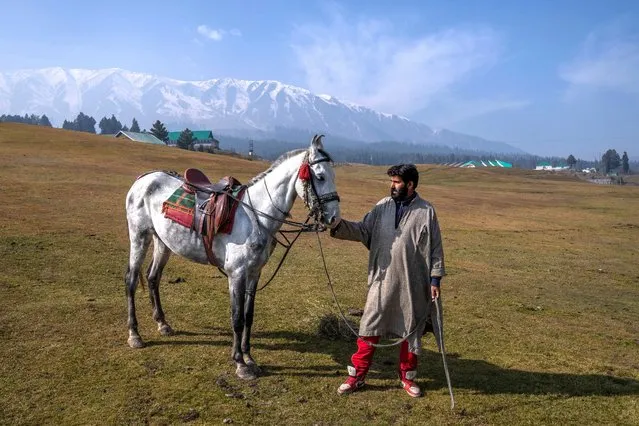 A Kashmiri man stands for a photograph along with his horse used for tourist rides in Gulmarg, northwest of Srinagar, Indian controlled Kashmir, Friday, November 4, 2022. (Photo by Dar Yasin/AP Photo)