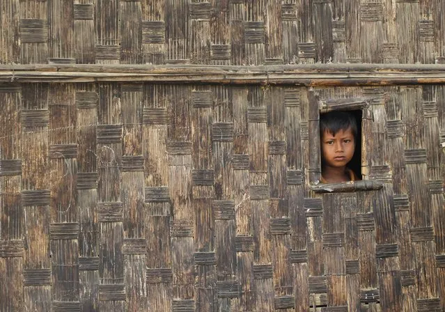 A boy looks from his temporary shelter at a Rohingya refugee camp as Myanmar's government embarks on a national census, in Sittwe April 2, 2014. At least 20,000 people in displacement camps around Sittwe will run out of drinking water within 10 days, while food stocks will run out within two weeks, imperilling thousands more. In the absence of nongovernment organisations (NGOs), the United Nations is working with the government to bring emergency supplies to camps, but that is only a short-term solution, said Pierre Peron, a spokesman for the UN Office for the Coordination of Humanitarian Affairs. (Photo by Soe Zeya Tun/Reuters)