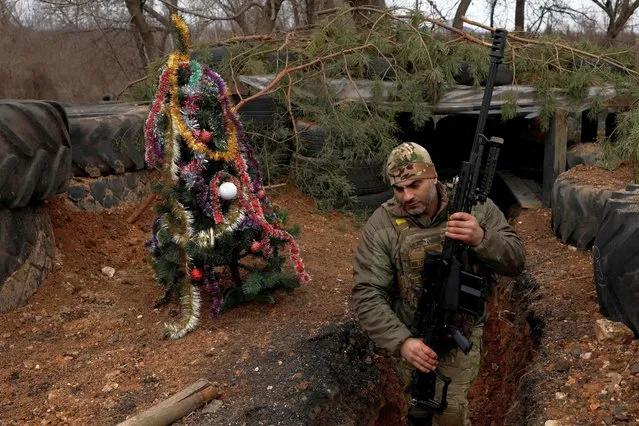 Ukrainian servicemen with the Dnipro-1 Special Tasks Patrol Police regiment Raphael Karapitian, 45, walks with weapons beside a decorated Christmas tree in the trenches on the front line, as Russia's attack on Ukraine continues, on Christmas Eve in Bakhmut, Ukraine on December 24, 2022. (Photo by Clodagh Kilcoyne/Reuters)
