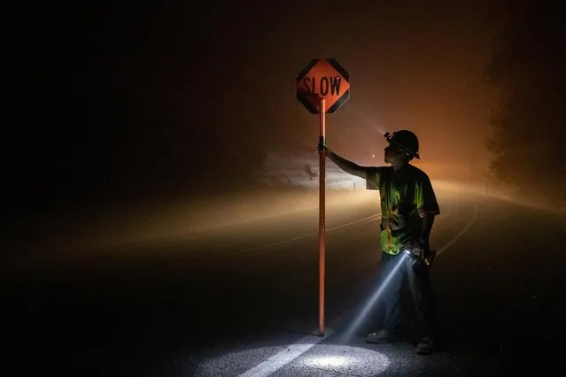 Bryan Alvarez holds a sign for oncoming traffic as utility workers repair power lines in the aftermath of the Obenchain Fire in Eagle Point, Oregon, U.S., September 11, 2020. (Photo by Adrees Latif/Reuters)