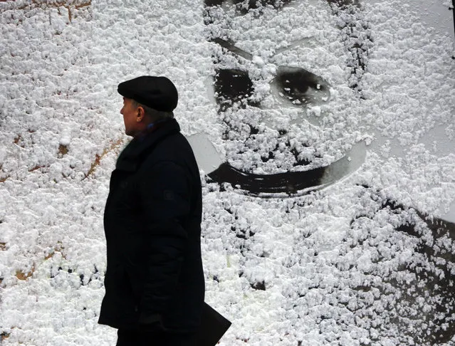 A man passes by a big board covered with snow in central Kiev, Ukraine, Friday, February 9, 2018. (Photo by Efrem Lukatsky/AP Photo)
