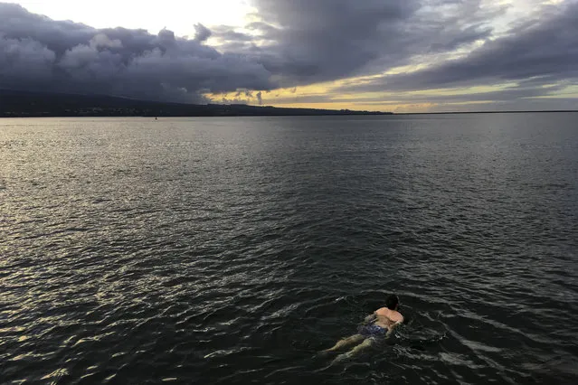 A man swims in the ocean in Hilo, Hawaii, Friday, May 11, 2018. Warnings that Hawaii's Kilauea volcano could shoot boulders and ash out of its summit crater are prompting people to rethink their plans to visit the Big Island. But most of the rest of the island is free of volcanic hazards, and local tourism officials are hoping travelers will recognize the Big Island is ready to welcome them. (Photo by Jae C. Hong/AP Photo)