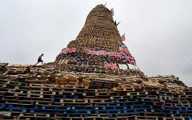 Mark Mayne,13, climbs up a huge bonfire built  at New Mossley on the outskirts of Belfast, Northern Ireland, on July 10, 2013. Hundreds of fires will be set alight at midnight on July 11 as Protestant loyalist's mark the defeat of the Catholic King James, by the Protestant William of Orange in 1690. (Photo by Paul Faith/PA)