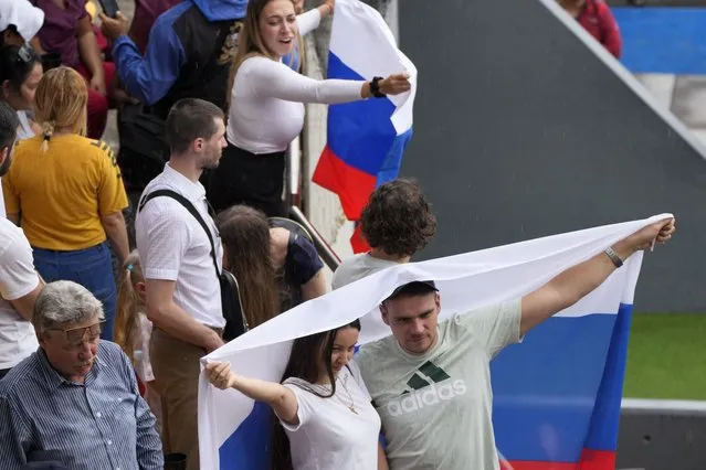 Spectators drape themselves with a Russian national flag during the Alba Games' opening ceremony, inside the baseball stadium in La Guaira, Venezuela, Friday, April 21, 2023. (Photo by Ariana Cubillos/AP Photo)