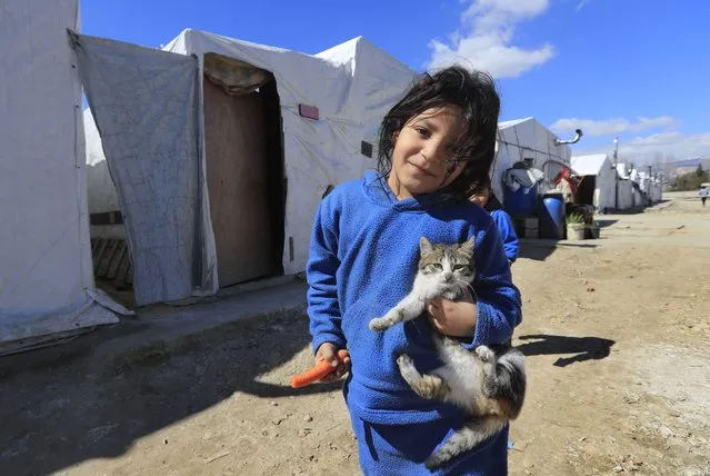 A displaced Syrian girl holds her cat, as she walks on an unpaved street at a refugee camp in Bar Elias, Bekaa Valley, Lebanon, Friday, March 5, 2021. UNICEF said Wednesday, March 10, 2021 that Syria’s 10-year-long civil war has killed or wounded about 12,000 children and left millions out of school in what could have repercussions for years to come in the country. The country's bitter conflict has killed nearly half a million people, wounded more than a million and displaced half the country’s population, including more than 5 million as refugees. (Photo by Hussein Malla/AP Photo)