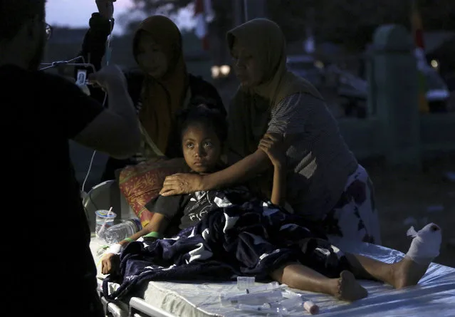 A doctor examines a child injured in the earthquake at a makeshift hospital in Tanjung, North Lombok, Indonesia, Tuesday, August 7, 2018. The north of Lombok was devastated by the powerful quake that struck Sunday night, damaging thousands of buildings and killing a large number of people. Rescuers were still struggling to reach all of the affected areas and authorities expect the death toll to rise. (Photo by Tatan Syuflana/AP Photo)