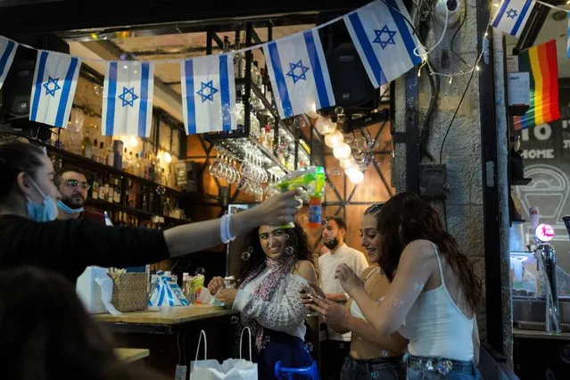 Israeli women check a selfie they took at a bar as they celebrate Independence Day at the Mahane Yehuda Market in Jerusalem, after more than a year of coronavirus restrictions, Wednesday, April 14, 2021. (Photo by Maya Alleruzzo/AP Photo)
