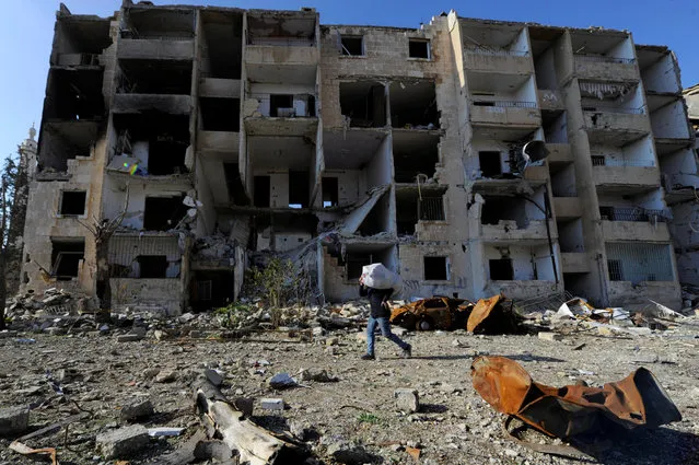 A man that came back to inspect his home carries his belongings near damaged buildings in goverment controlled Hanono housing district in Aleppo, Syria December 4, 2016. (Photo by Omar Sanadiki/Reuters)