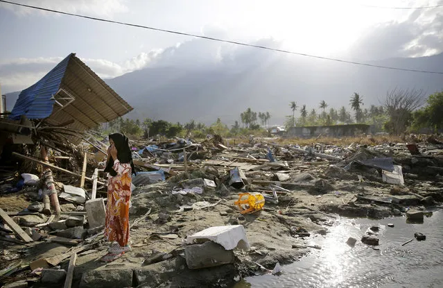 In this October 4, 2018, photo, a woman walks past toppled structures along a busy road in the earthquake and tsunami-damaged Palu, Central Sulawesi, Indonesia. The 7.5 magnitude quake triggered not just a tsunami that leveled huge swathes of the region's coast, but a geological phenomenon known as liquefaction, making the soil move like liquid and swallowing entire neighborhoods. (Photo by Aaron Favila/AP Photo)