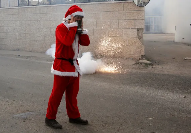 A Palestinian protester, dressed as Santa Claus, reacts to a sound grenade fired by Israeli troops during clashes at a protest in the West Bank city of Bethlehem, December 23, 2016. (Photo by Mussa Qawasma/Reuters)
