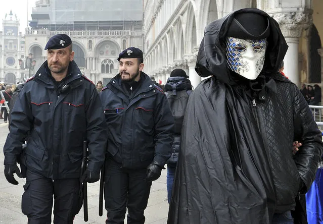 A mask crosses St. Mark's Square as police officers patrol on the occasion of the Venice Carnival, in Venice, Italy, Saturday, January 30, 2016. (Photo by Luigi Costantini/AP Photo)