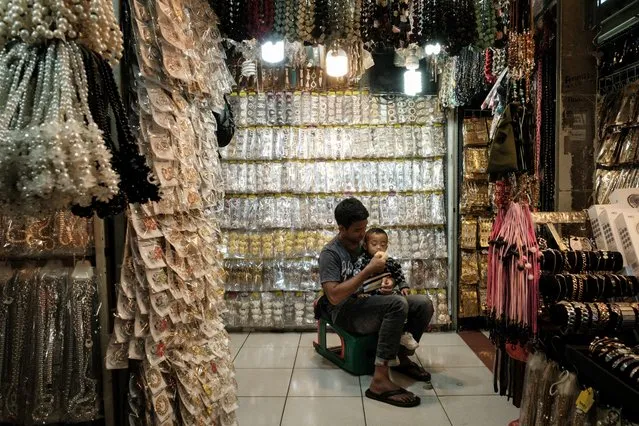 A man feeds his one-year-old son at Tanah Abang Market, Southeast Asia's largest wholesale shopping center for garment and textile, in Jakarta on September 28, 2023. (Photo by Yasuyoshi Chiba/AFP Photo)