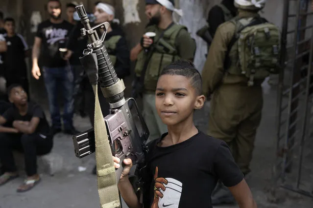 A Palestinian kid poses with an M-16 rifle during the funeral of Qasim Qasim, 23, in the West Bank city of Tulkarem, Saturday, October 14, 2023. Qasim was killed in clashes with Israeli forces on Friday following a demonstration supporting the Gaza Strip. (Photo by Majdi Muhammad/AP Photo)
