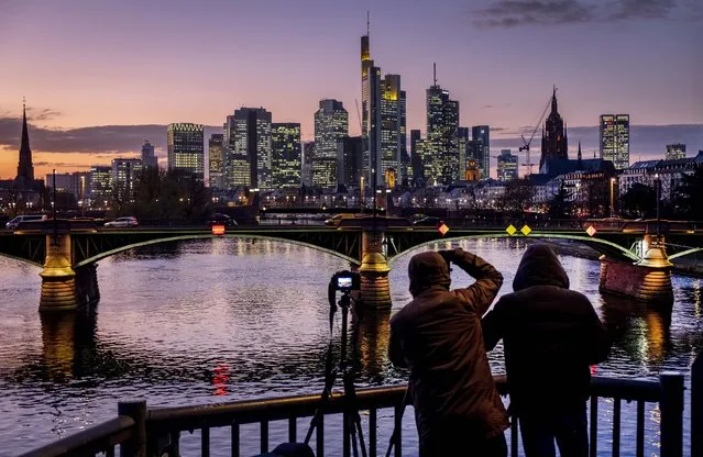 Two men take photographs of the buildings of the banking district in Frankfurt, Germany, after sunset on Friday, November 29, 2019. (Photo by Michael Probst/AP Photo)