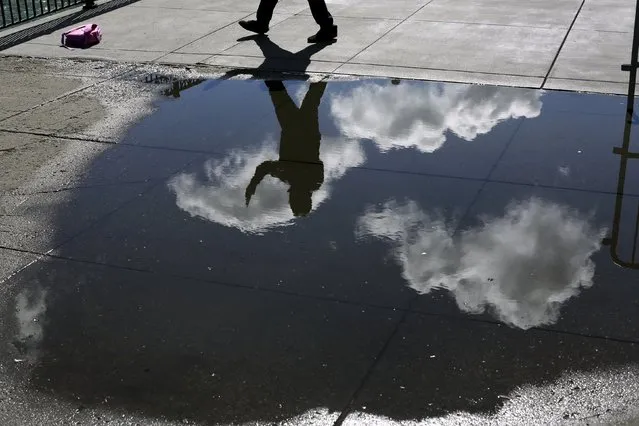 A pedestrian snaps a photograph while reflected in a rain puddle along The Embarcadero in San Francisco, California April 7, 2015. (Photo by Robert Galbraith/Reuters)