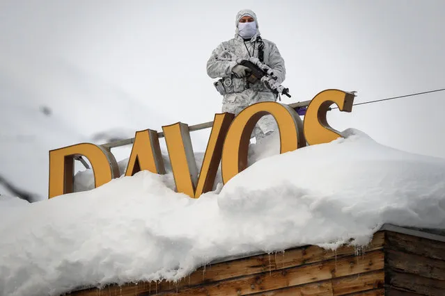 A policeman wearing camouflage clothing stands on the rooftop of a hotel, next to letters covered in snow reading “Davos”, near the Congress Centre ahead of the World Economic Forum (WEF) annual meeting on January 21, 2019 in Davos, eastern Switzerland. (Photo by Fabrice Coffrini/AFP Photo)