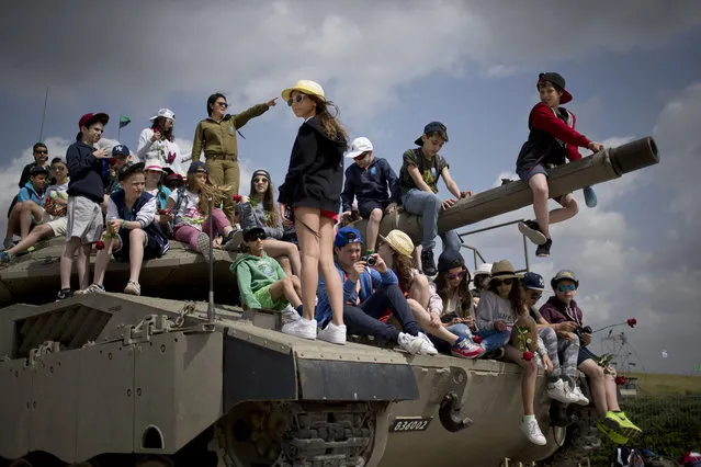 School children from Belgium sit on a tank on display as they listen to an Israeli soldier speaks about Israel's wars, near the wall of names of fallen soldiers, at the Armored Corps memorial, before a ceremony marking the annual Memorial Day for soldiers and civilians killed in more than a century of conflict between Jews and Arabs, in Latrun near Jerusalem, Israel, Wednesday, April 22, 2015. (Photo by Ariel Schalit/AP Photo)