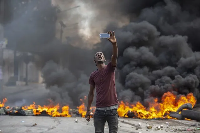 A protester takes a selfie at a burning barricade set by protesters in Port-au-Prince, Haiti, Monday, October 18, 2021. Workers angry about the nation’s lack of security went on strike in protest two days after 17 members of a U.S.-based missionary group were abducted by a violent gang. (Photo by Joseph Odelyn/AP Photo)