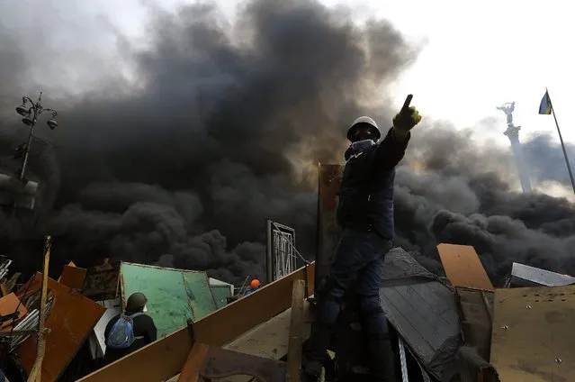 An anti-government protester calls upon his comrades to advance over a burning barricade in Kiev's Independence Square February 20, 2014. (Photo by Yannis Behrakis/Reuters)