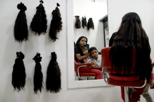 In this April 2, 2019 photo, Nelly Navarro sits with her kids Nerianny and Luis in a beauty salon where she came to consult how much money she could get for her hair, in Caracas, Venezuela. Navarro said she needs the $100 to travel to Colombia where she's planning to move. (Photo by Natacha Pisarenko/AP Photo)