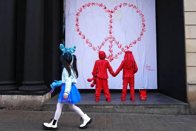 A little girl walks past a newly installed sculpture, by French street artist James Colomina, which depicts two kids holding hands, one of them wears a Jewish kippah while the other wears a Palestinian keffiyeh, and looking at a heart-shaped CND peace sign made with red hand prints, in Barcelona on February 8, 2024. (Photo by Pau Barrena/AFP Photo)