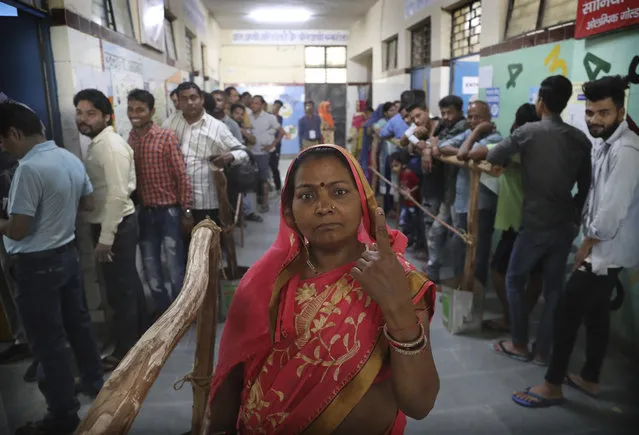 A woman displays indelible ink mark on her finger after casting her vote as others wait in queue in New Delhi, India, Sunday, May 12, 2019. Indians are voting in the next-to-last round of 6-week-long national elections, marked by a highly acrimonious campaign with Prime Minister Narendra Modi flaying the opposition Congress party rival Rahul Gandh's family for the country's ills. (Photo by Manish Swarup/AP Photo)