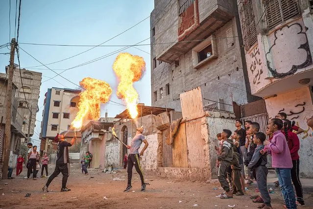 Palestinian youth perform a show with fire in front of people in Al-Shejaiya neighborhood on November 14, 2021 in Gaza City, Gaza. For many young people living in Gaza, the years of living under a blockade effectively cutting them off from the outside world has taken a heavy toll with mental health levels rising among young people. The constant struggle of living with food and water insecurities and regular power outages, skyrocketing youth unemployment and rising suicide rates especially amongst men aged 18-30, many young people turn to sport and other recreational activities to relieve the pressures of everyday life, from boxing to horse riding many young people have found creative outlets to help release mental stress. (Photo by Fatima Shbair/Getty Images)