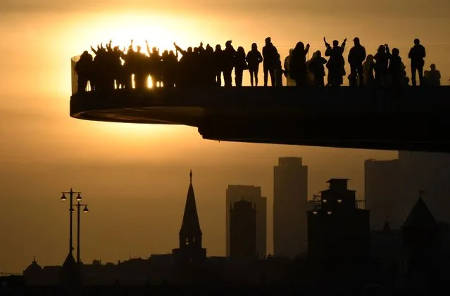 People enjoy sunset from a pedestrian bridge at the Zaryadye Park in central Moscow on March 22, 2024. (Photo by Olga Maltseva/AFP Photo)