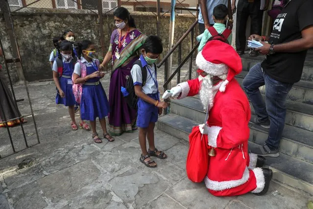 A man dress as Santa Claus checks the temperature of students as they arrive to attend classes at a school in Mumbai, India, Wednesday, December 15, 2021. After being closed for nearly-20-months due to the coronavirus pandemic, schools in Mumbai reopened for classes 1 to 7 Wednesday. (Photo by Rafiq Maqbool/AP Photo)
