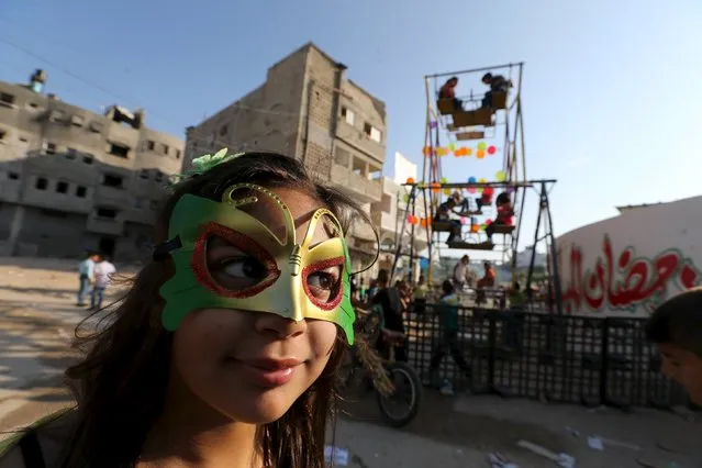 A Palestinian girl wears a mask as children enjoy a ride on a ferris wheels on the first day of Eid al-Fitr holiday, marking the end of the holy month of Ramadan, in the east of Gaza City, July 17, 2015. (Photo by Ibraheem Abu Mustafa/Reuters)