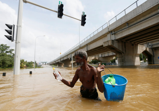 A man carries water and food in a bucket as they walk through a flooded road in Kaduwela, Sri Lanka May 20, 2016. (Photo by Dinuka Liyanawatte/Reuters)