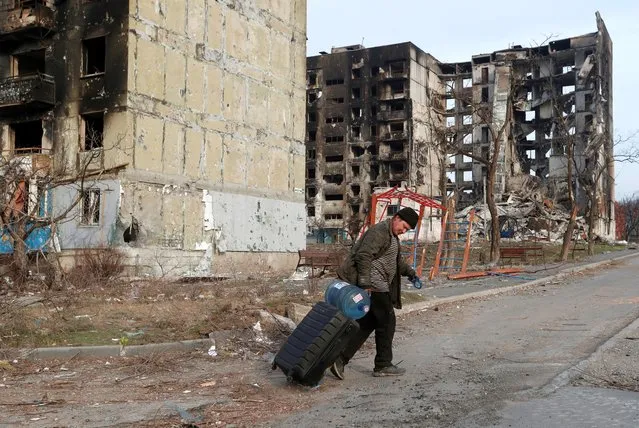 A local resident walks with a suitcase past apartment buildings destroyed during Ukraine-Russia conflict in the besieged southern port city of Mariupol, Ukraine March 30, 2022. (Photo by Alexander Ermochenko/Reuters)