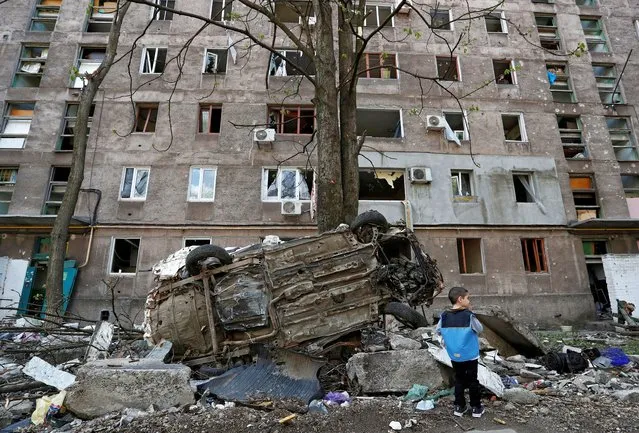 A boy stands next to a wrecked vehicle in front of an apartment building damaged during Ukraine-Russia conflict in the southern port city of Mariupol, Ukraine on April 24, 2022. (Photo by Alexander Ermochenko/Reuters)