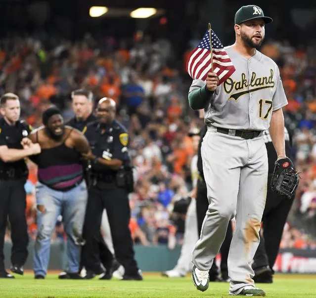 Oakland Athletics first baseman Yonder Alonso (17) holds a United States flag as a spectator, back left, is arrested by police officers for running onto the field during the fourth inning of a baseball game against the Houston Astros, Saturday, June 4, 2016, in Houston. (Photo by Eric Christian Smith/AP Photo)
