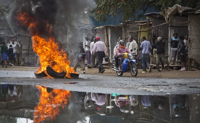 A motorcyclist drives past a barricade of burning tyres, erected by demonstrators calling for the disbandment of the national electoral commission over allegations of bias and corruption, in the Kibera slum of Nairobi, Kenya Monday, June 6, 2016. (Photo by Ben Curtis/AP Photo)