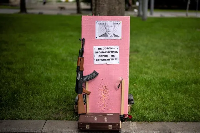 A plastic Kalashnikov rifle to shoot balls at a portrait of Russian President Vladimir Putin, is photographed at a street attraction in the centre of Lviv, Ukraine on Saturday, May 14, 2022. The banner reads in Ukrainian: It's not a shame to miss. It's a shame not to try to shoot! Glory to Ukraine, Death to our enemies!. (Photo by Emilio Morenatti/AP Photo)