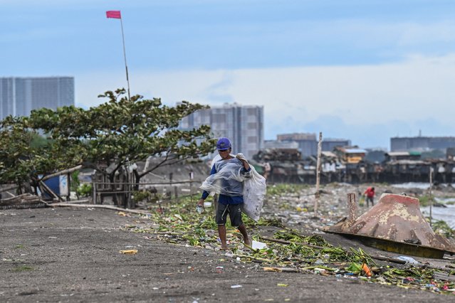 A man wearing a raincoat collects trash despite the wind brought by Tropical Storm Trami, in Manila on October 23, 2024. (Photo by Jam Sta Rosa/AFP Photo)