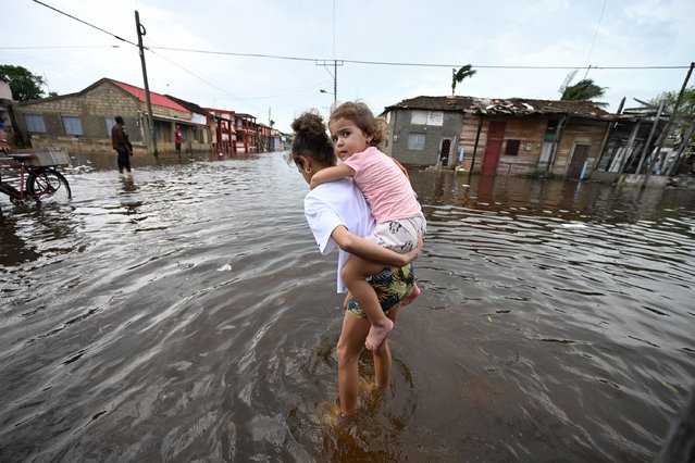 A girl carries a toddler through a flooded street after the passage of Hurricane Rafel in Batabano, Mayabeque province, Cuba, on November 7, 2024. (Photo by Yamil Lage/AFP Photo)